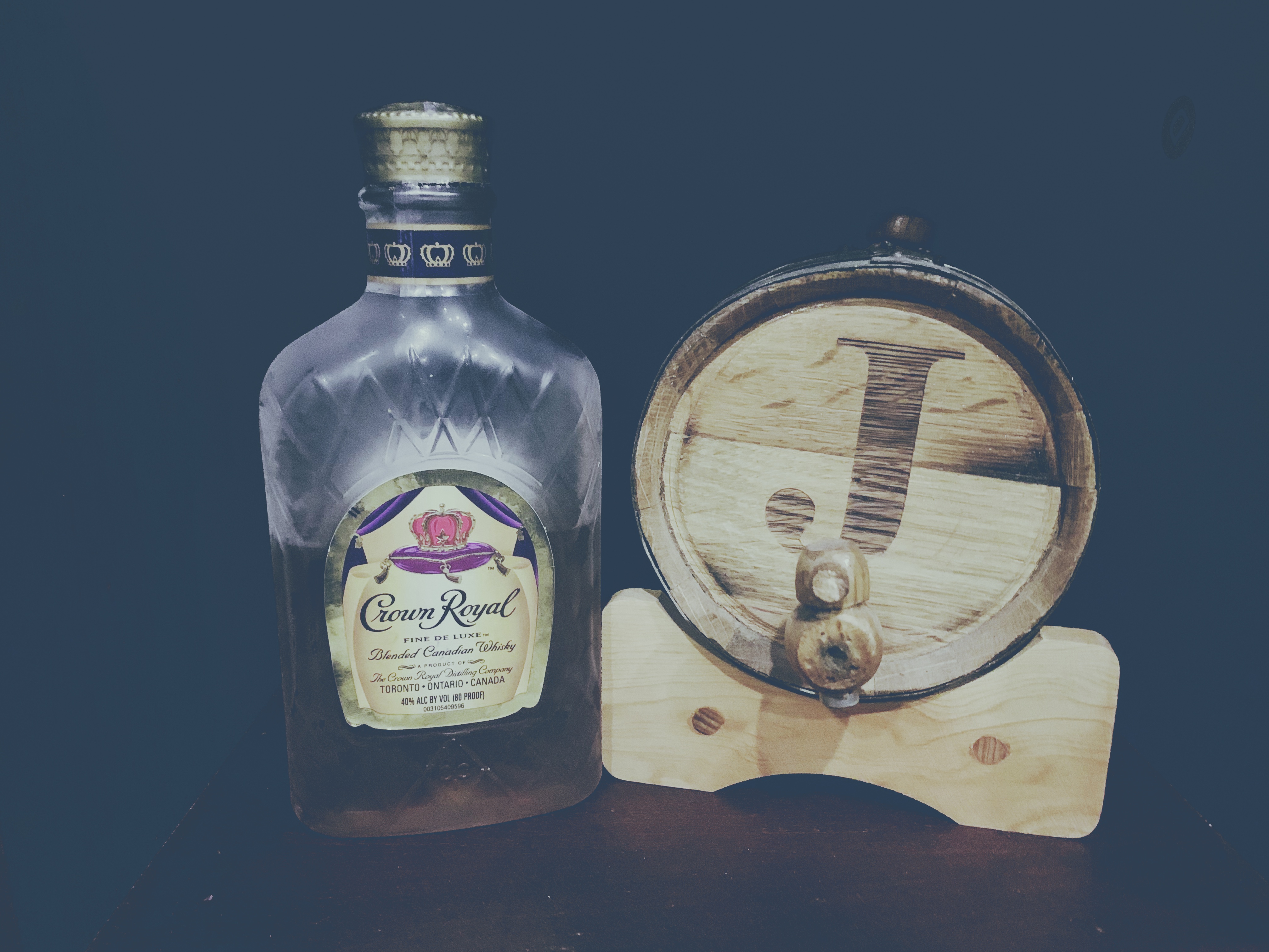Crown Royal bottle beside a small wooden barrel engraved with the letter J
