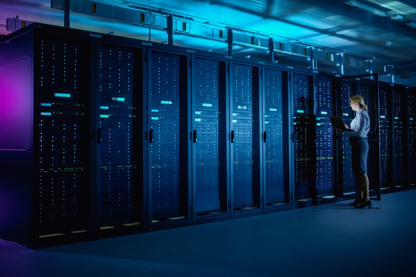 Engineer with a laptop standing beside rows of server racks in a data center